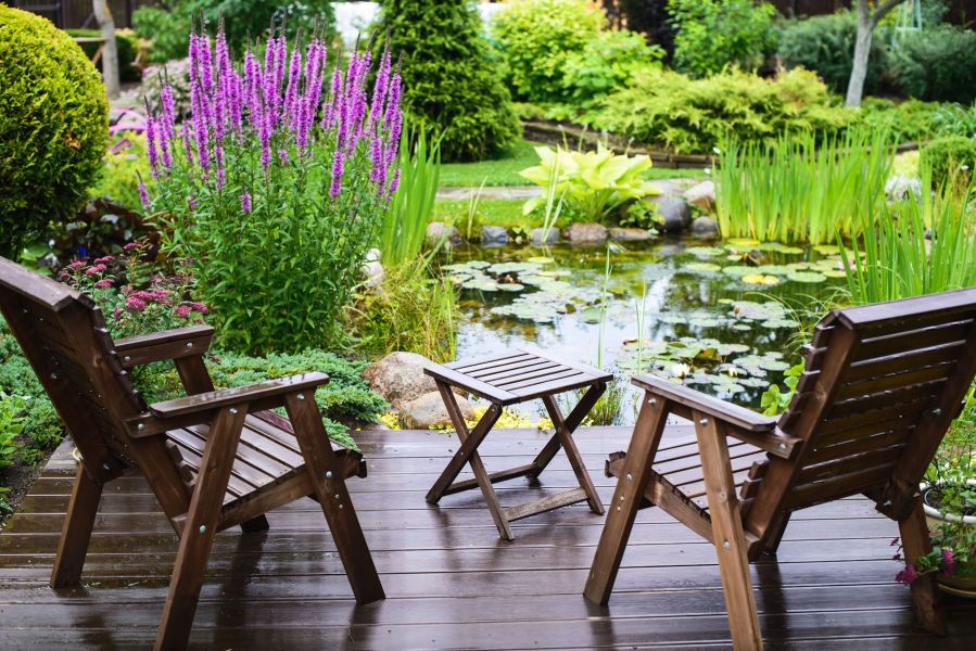 Ausblick von einer Terrasse mit 2 Holzstühlen auf traumhaft angelegten Gartenteich